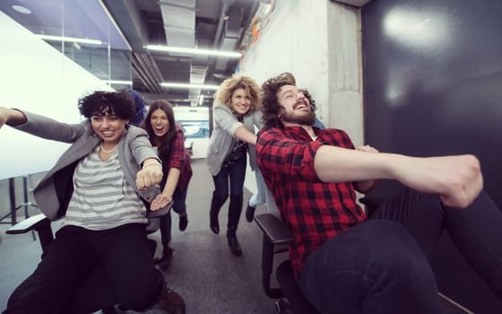 multiethnics startup business team of software developers having fun while racing on office chairs,excited diverse employees laughing enjoying funny activity at work break, creative friendly workers playing game together