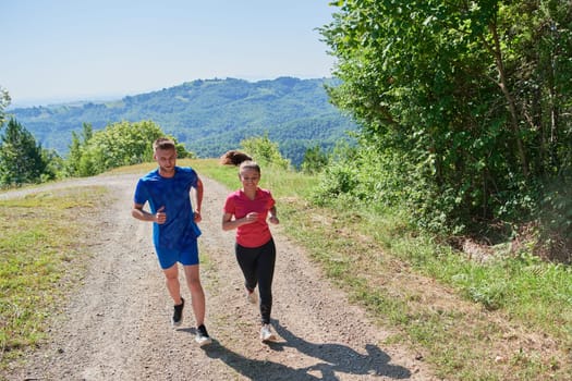 young happy couple enjoying in a healthy lifestyle while jogging on a country road through the beautiful sunny forest, exercise and fitness concept