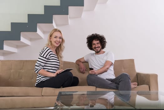 Young couple relaxes on the sofa in the luxury living room, using a tablet and remote control