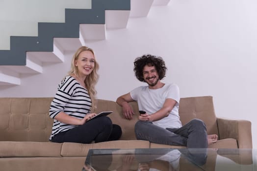 Young couple relaxes on the sofa in the luxury living room, using a tablet and remote control