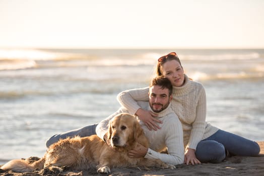 Couple With A Dog enjoying time  together On The Beach at autumn day