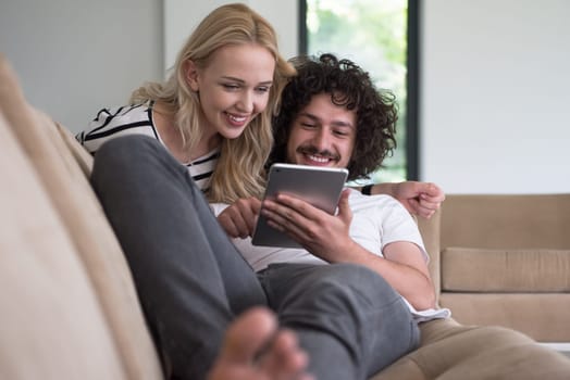 Young couple relaxing at luxurious home with tablet computers reading in the living room on the sofa couch.