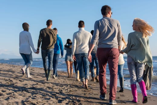 group of young friends spending day together running on the beach during autumn day