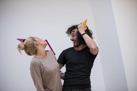 Young happy couple in party hats blowing in whistle isolated on a white background