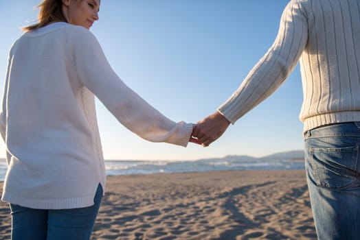 Young couple having fun walking and hugging on beach during autumn sunny day