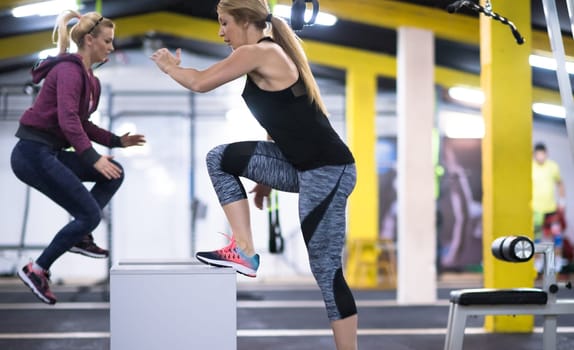 group of young healthy athletic people training jumping on fit box at cross fitness gym