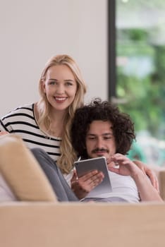Young couple relaxing at luxurious home with tablet computers reading in the living room on the sofa couch.
