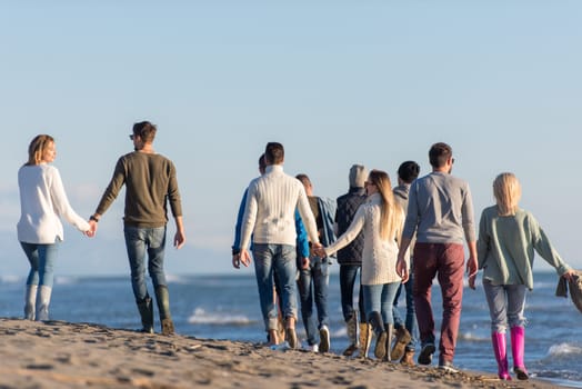 group of young friends spending day together running on the beach during autumn day