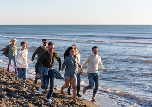 group of young friends spending day together running on the beach during autumn day