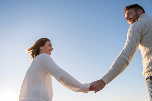 Young couple having fun walking and hugging on beach during autumn sunny day