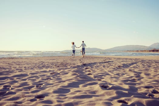 Couple Running On The Beach Holding Their Hands with dog On autmun day