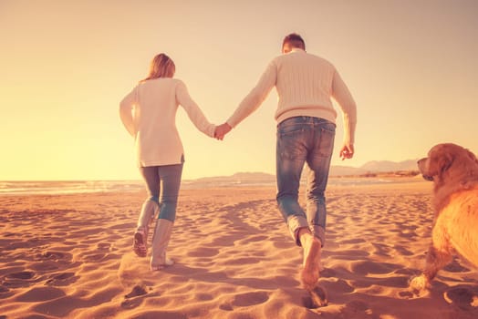 Couple Running On The Beach Holding Their Hands with dog On autmun day