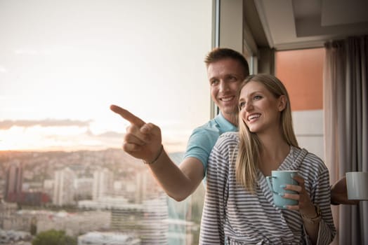 romantic happy young couple enjoying evening coffee and beautiful sunset landscape of the city while standing by the window