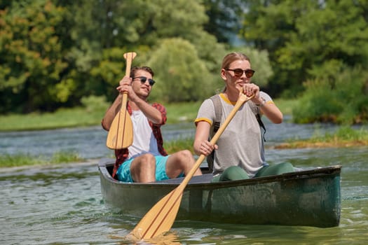 Couple adventurous explorer friends are canoeing in a wild river surrounded by the beautiful nature