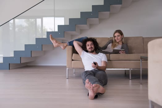 Young couple relaxes on the sofa in the luxury living room, using a tablet and remote control