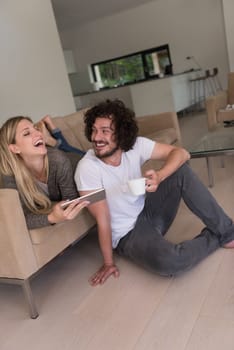 Young couple relaxing at luxurious home with tablet computers reading in the living room on the sofa couch.