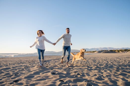 Couple Running On The Beach Holding Their Hands with dog On autmun day