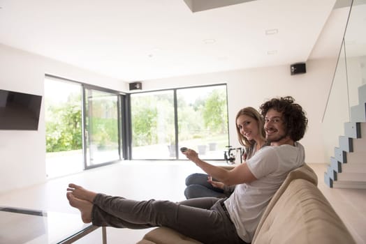 Young couple relaxes on the sofa in the luxury living room, using a tablet and remote control