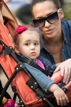 portrait of a beautiful young mother with sunglasses and a baby in a stroller on a sunny day in the park