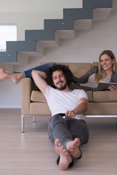 Young couple relaxes on the sofa in the luxury living room, using a tablet and remote control