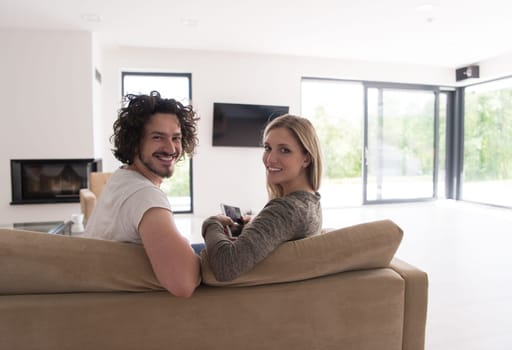 Rear view of couple watching television in living room their luxury home