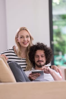 Young couple relaxing at luxurious home with tablet computers reading in the living room on the sofa couch.