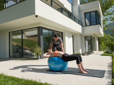 young beautiful woman and personal trainer doing exercise with pilates ball in front of her luxury home