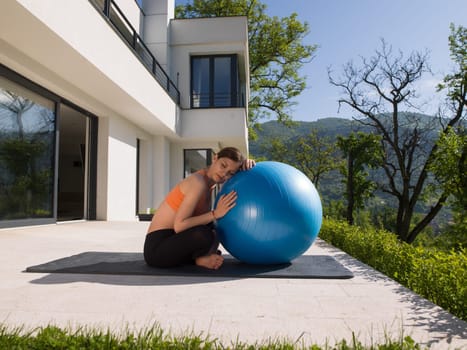 young beautiful woman doing exercise with pilates ball in front of her luxury home villa