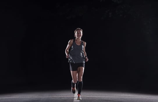 fit muscular female runner training for marathon running at night on beautiful road in nature.