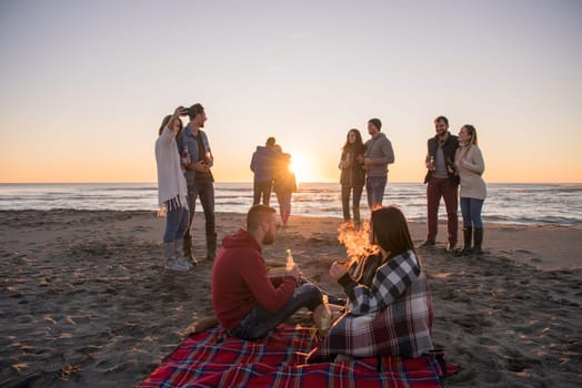 Young Couple enjoying with friends Around Campfire on The Beach At sunset drinking beer