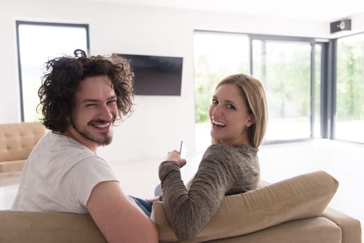 Rear view of couple watching television in living room their luxury home