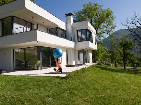young beautiful woman doing exercise with pilates ball in front of her luxury home villa