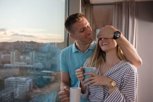 romantic happy young couple enjoying evening coffee and beautiful sunset landscape of the city while standing by the window