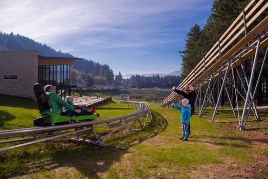 Happy family driving on alpine coaster during beautiful sunny day in the nature