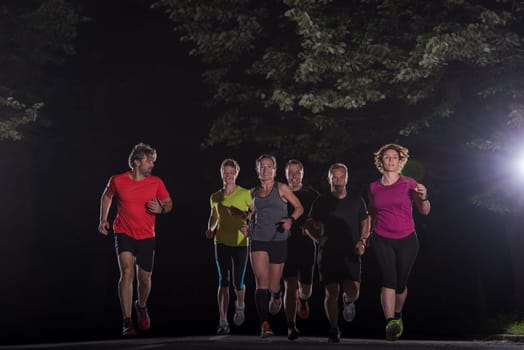 group of healthy people jogging in city park, runners team at night training