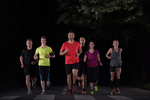 group of healthy people jogging in city park, runners team at night training
