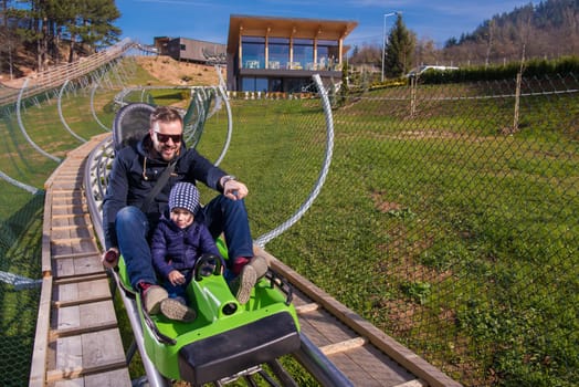 Excited young father and son driving on alpine coaster while enjoying beautiful sunny day in the nature