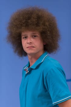 portrait of a young man with a funky hairstyle with arms crossed on blue background