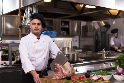 chef using ax while cutting big piece of beef  on wooden board in restaurant kitchen