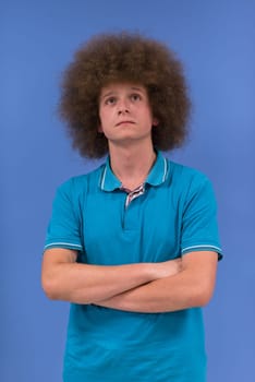 portrait of a young man with a funky hairstyle with arms crossed on blue background