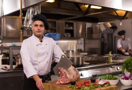 chef using ax while cutting big piece of beef  on wooden board in restaurant kitchen