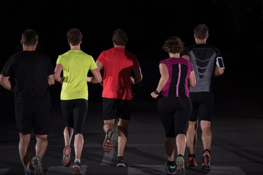 group of healthy people jogging in city park, runners team at night training