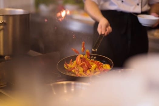 Young male chef flipping vegetables in wok at commercial kitchen