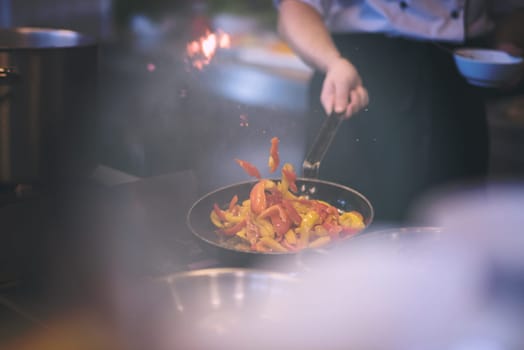 Young male chef flipping vegetables in wok at commercial kitchen