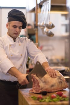 chef using ax while cutting big piece of beef  on wooden board in restaurant kitchen