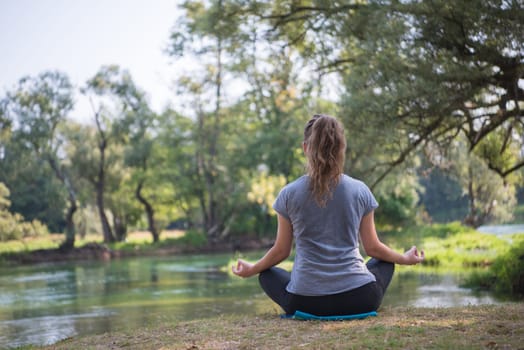 healthy woman relaxing while meditating and doing yoga exercise in the beautiful nature on the bank of the river