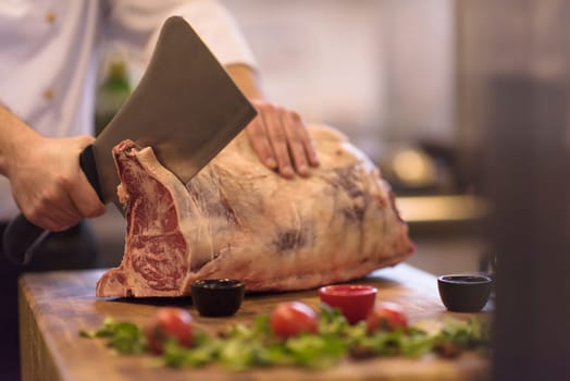 chef using ax while cutting big piece of beef  on wooden board in restaurant kitchen