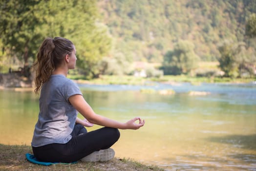 healthy woman relaxing while meditating and doing yoga exercise in the beautiful nature on the bank of the river