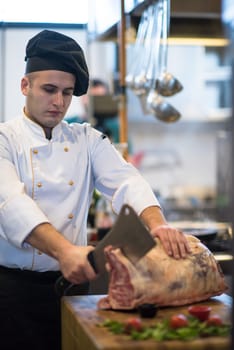 chef using ax while cutting big piece of beef  on wooden board in restaurant kitchen