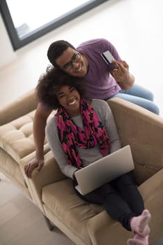 Happy young african american couple shopping online through laptop using credit card at home
